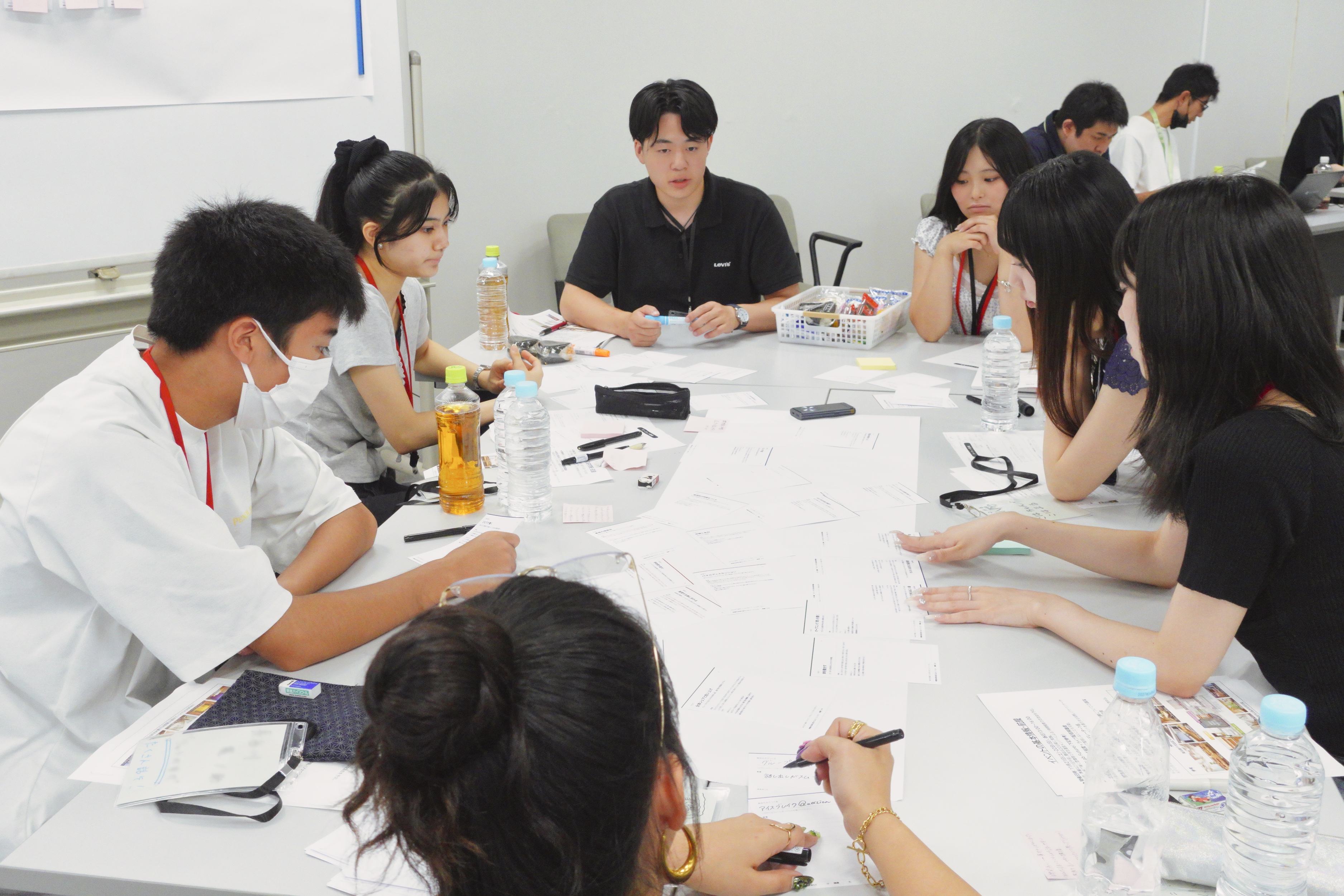 7人の学生が机の周りを囲んで座り話し合っている様子