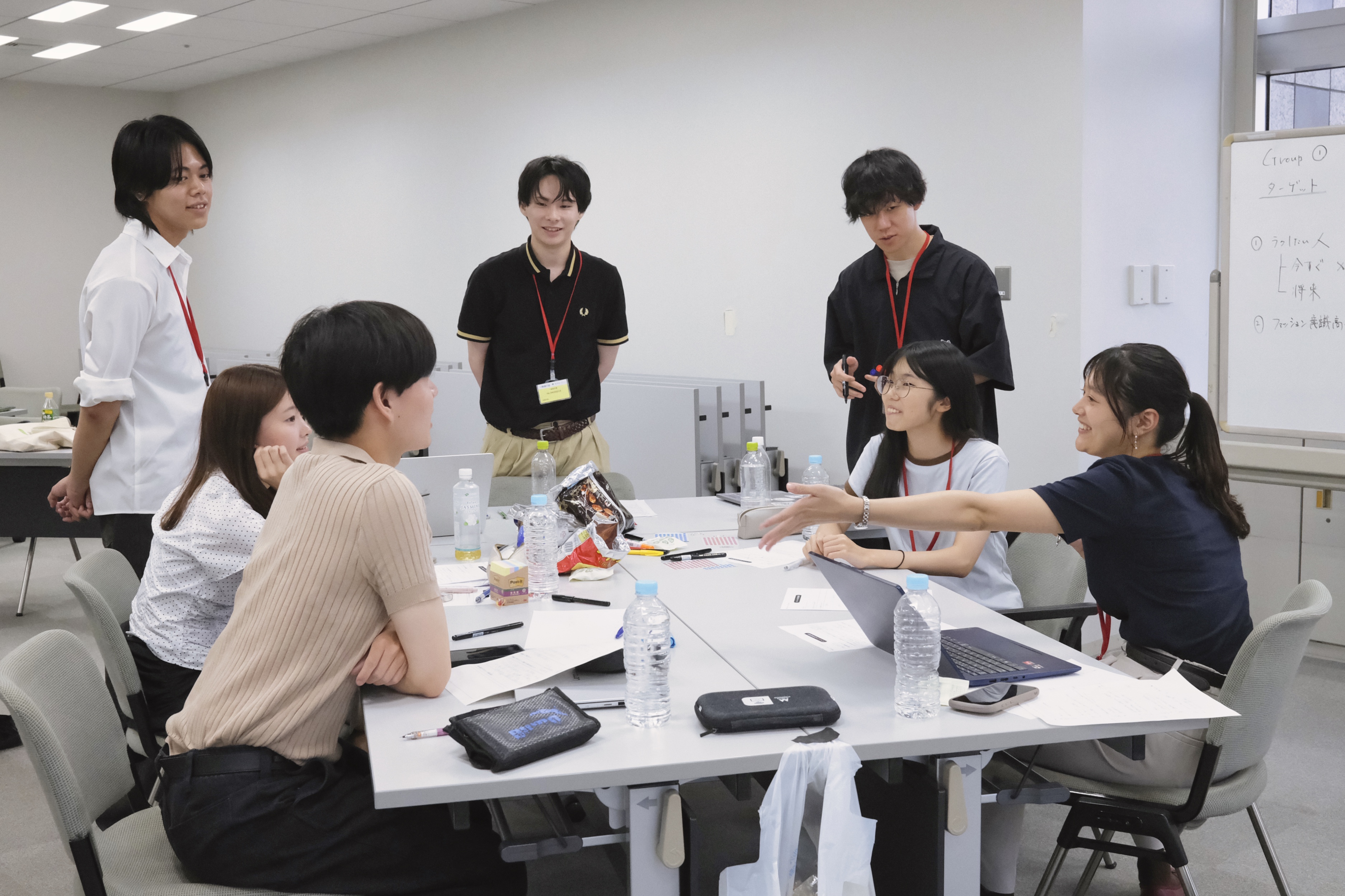 学生運営メンバー4人が席に座り3人が立って話し合っている様子